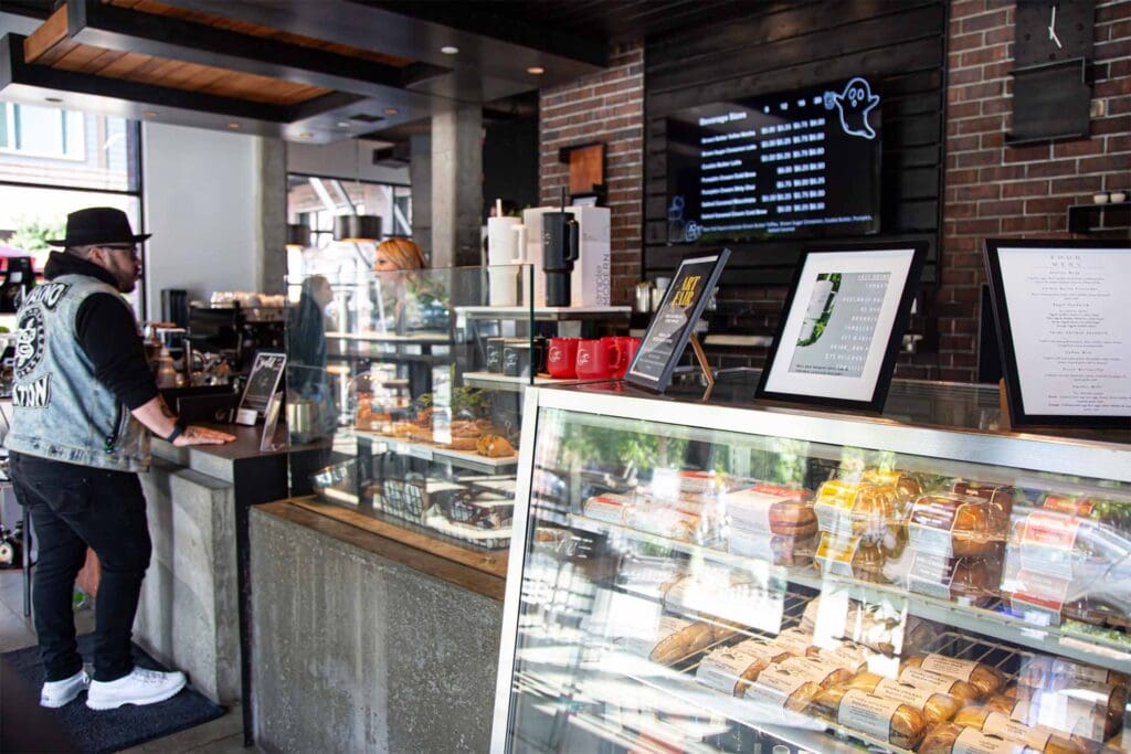 Inside view of the Kirkland coffee shop featuring a food display case, large menu on the wall, and a customer ordering